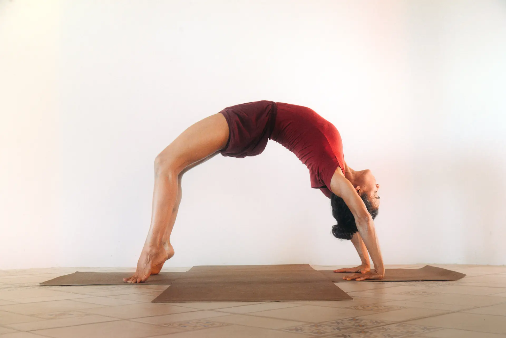 Juliana Lião em postura de arco, Urdhva Dhanurasana, em tapete no chão claro